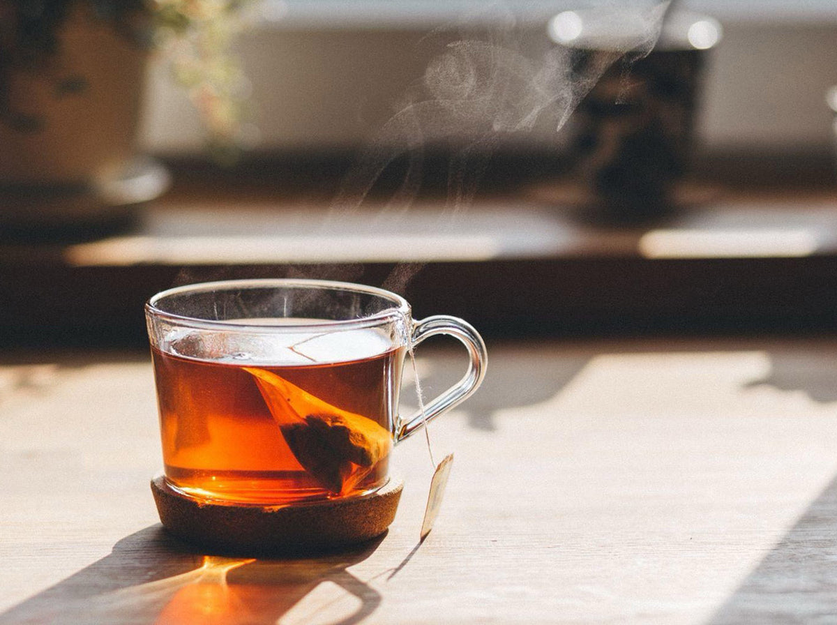 closeup of steaming hot tea in clear mug on wooden table